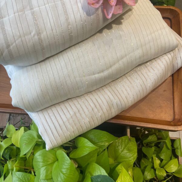 An ethereal Ivory Offwhite Running fabric in pure viscose georgette with beautiful lurex lines throughout in a beautiful vertical design giving it a stunning feel! The fabric can be cut in meterage as per your requirement. The fabric with tiny embroidery is ideal to converted as saree , suit or frock & is entirely dyeable to the shade of your choice