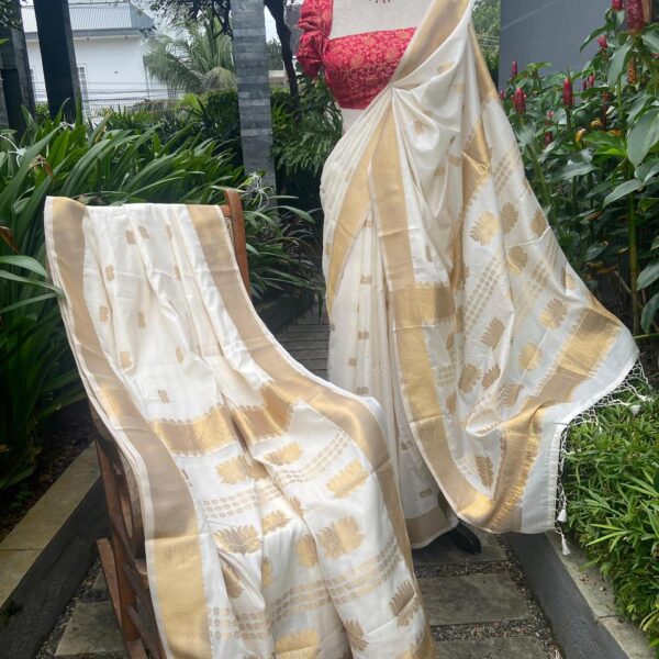 A stunningly beautiful Dola Silk saree with a beautiful weave of Antique Gold Lotus & floral butta weaving creating a stunning visual impact. With blouse self with borders. The ethereal antique Ivory Gold hue of the saree creates a beautiful drape once worn ensuring you steal the show this Onam ! (The displayed blouse is customised additionally)